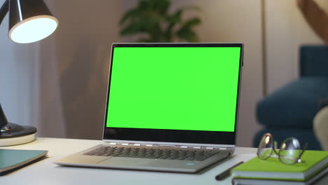 open-laptop-with-green-screen-on-working-table-in-living-room-man-is-turning-off-lamp-at-background-zoom-shot-approaching-to-chroma-key-display